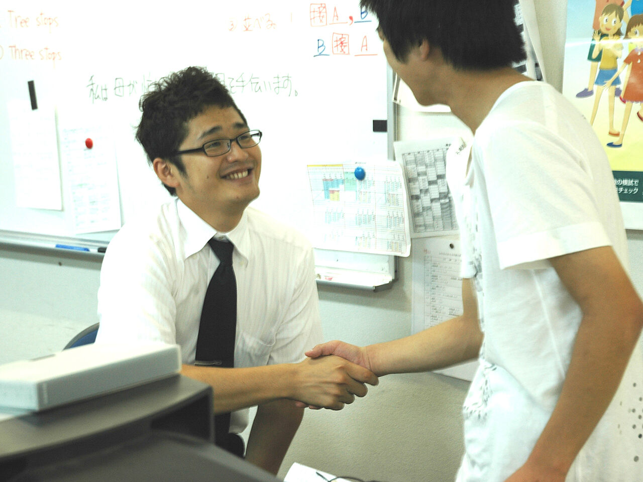 先生が生徒に笑顔で握手している様子