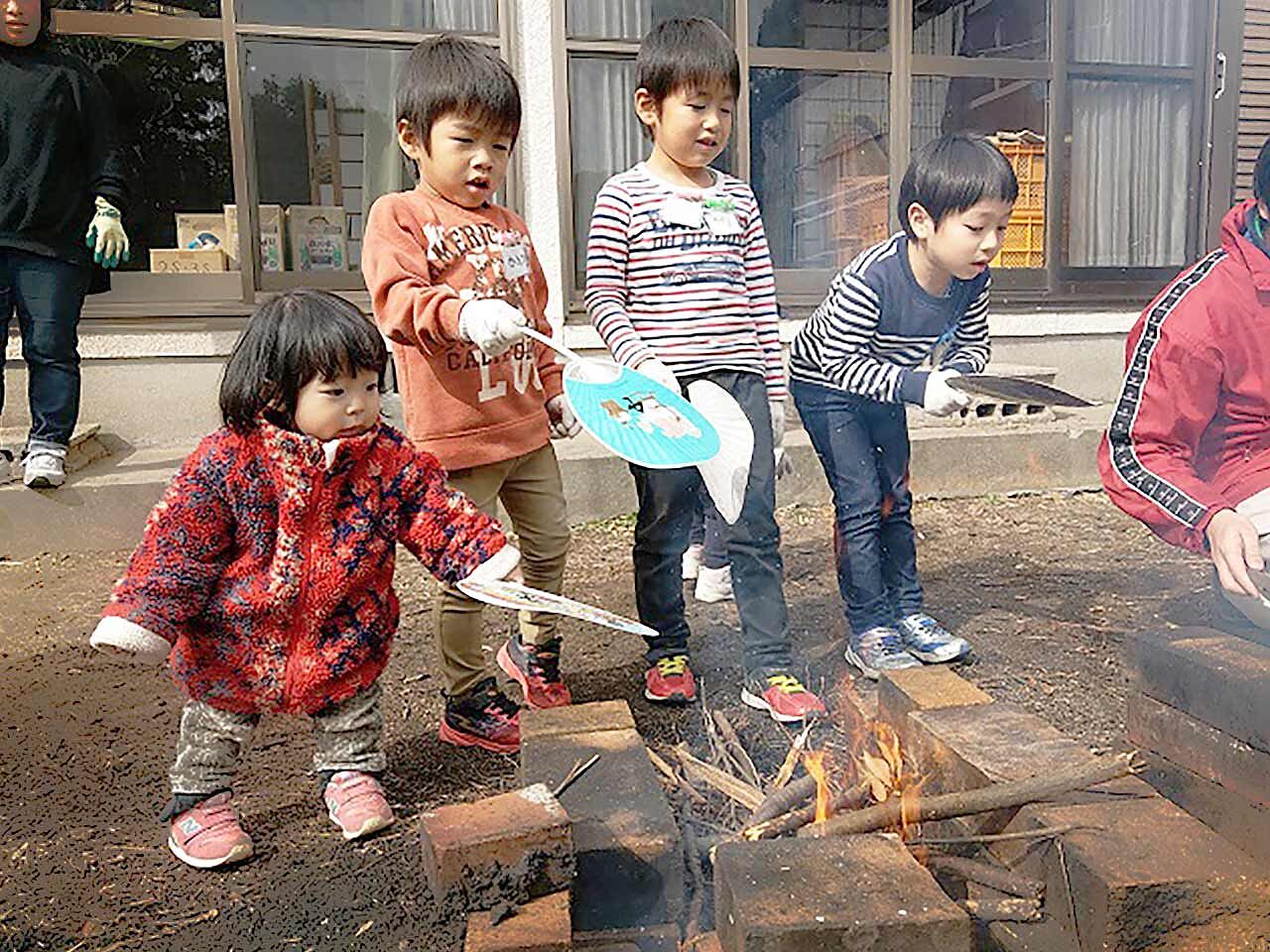 子どもたちがうちわで火を仰いでいる画像