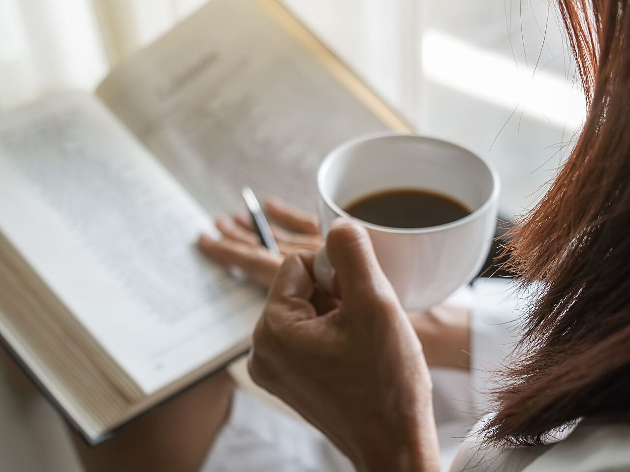 コーヒーを飲みながら読書をしている女性の画像