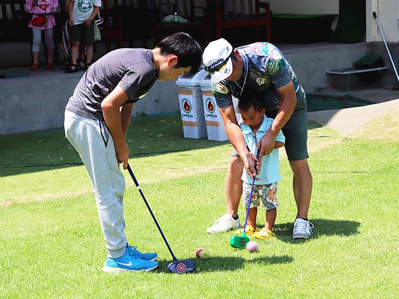 小さい子どもがゴルフの指導を受けている画像