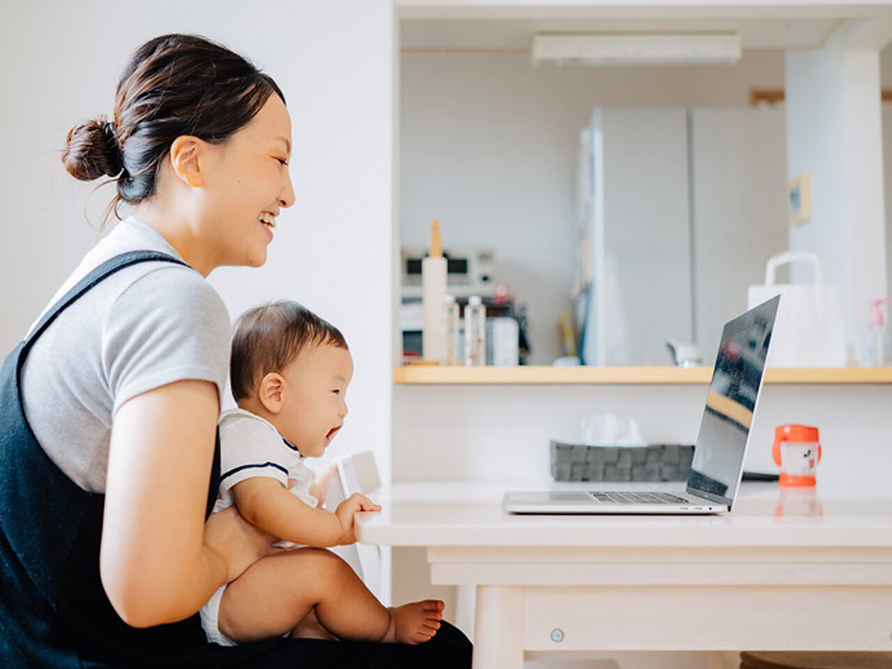 お母さんが赤ちゃんを抱いてパソコンの前にいる画像