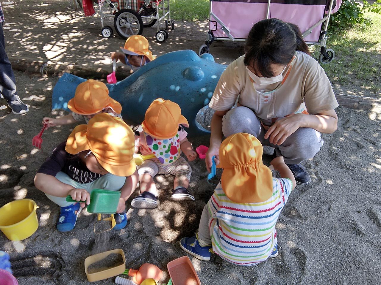 園内で子どもたちと保育士が砂場で遊んでいる画像