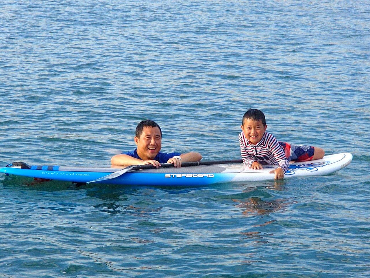 お父さんと子どもがボードにつかまり海に浮いている画像