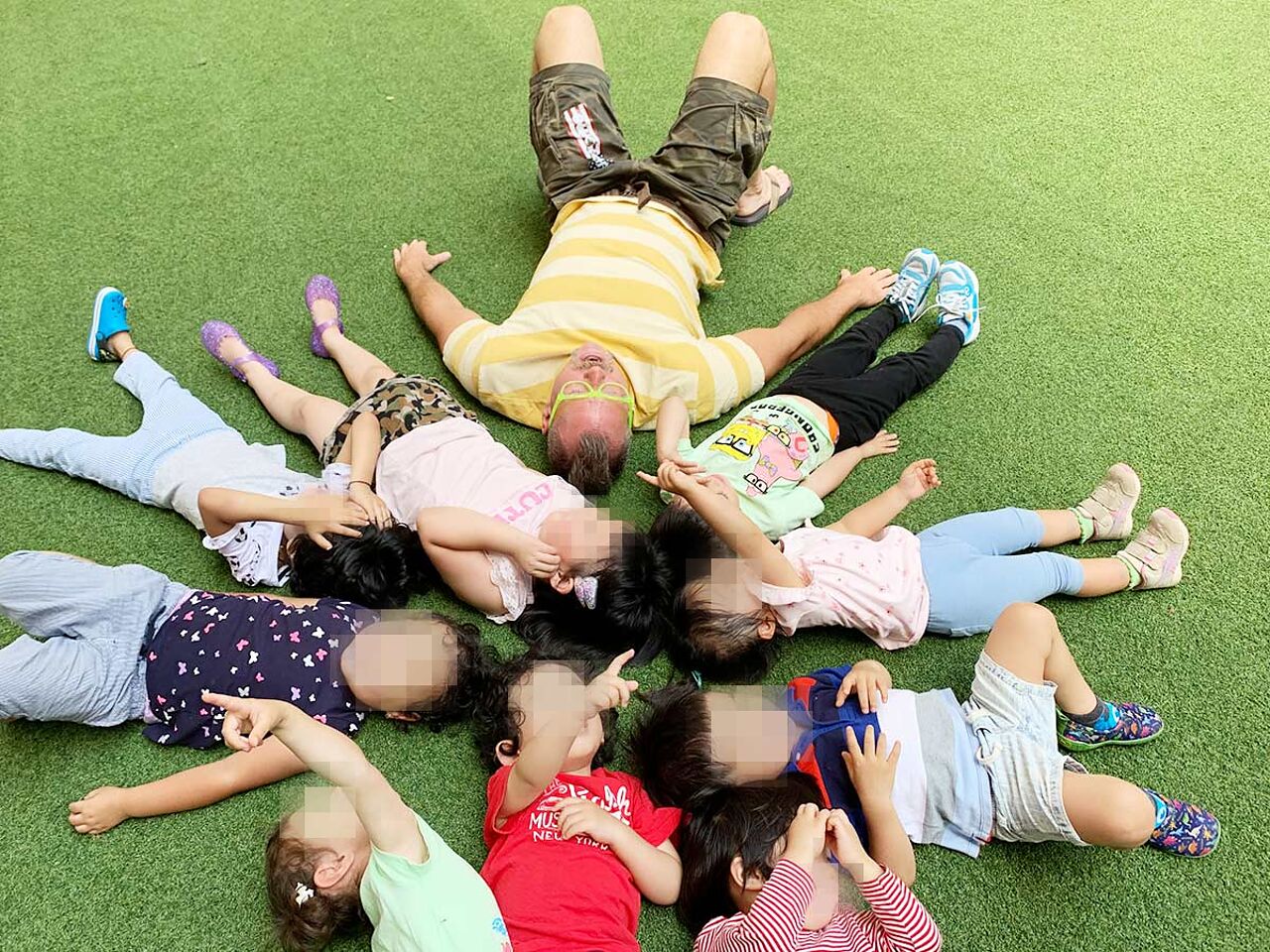 子どもたちと講師が芝生の上で寝転んでいる画像