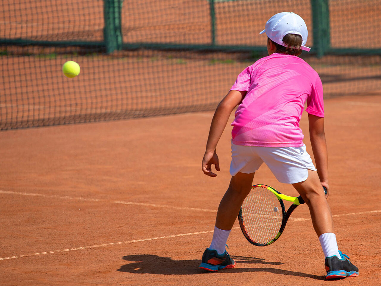 ピンクのTシャツを着た男の子がテニスをしている画像