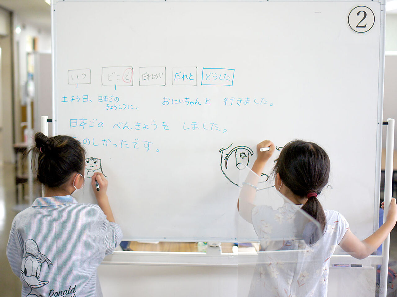 子ども2人がホワイトボードに文字を書いている画像
