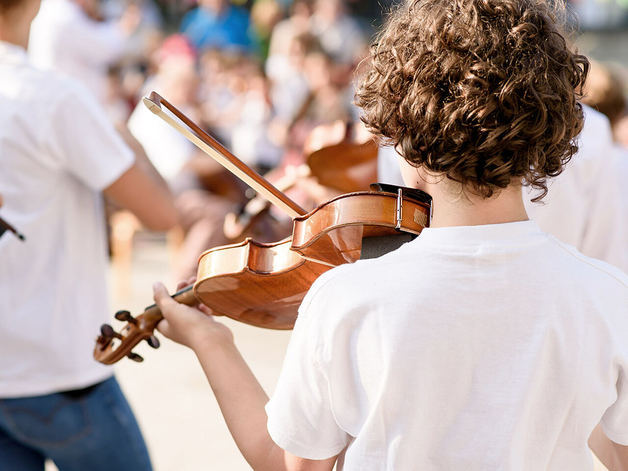 大勢の前でバイオリンを弾く男の子の後ろ姿の画像
