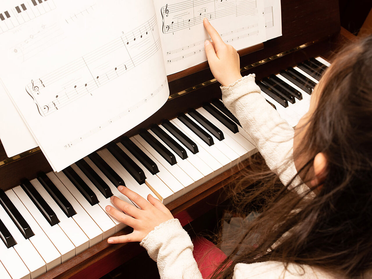 女の子が楽譜を見ながらピアノを弾いている画像