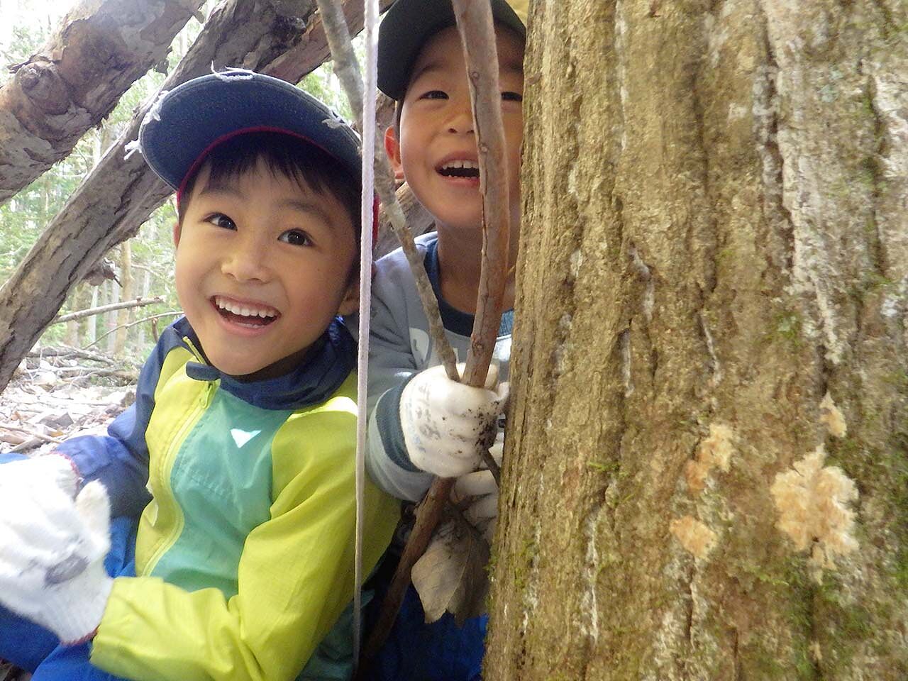 木の横で笑っている子どもの画像