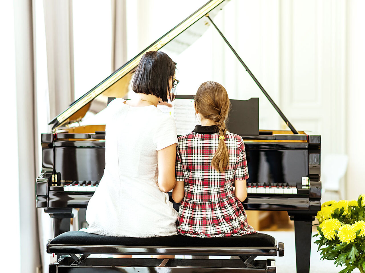 女の子が女性講師にピアノの指導を受けている後ろ姿の画像