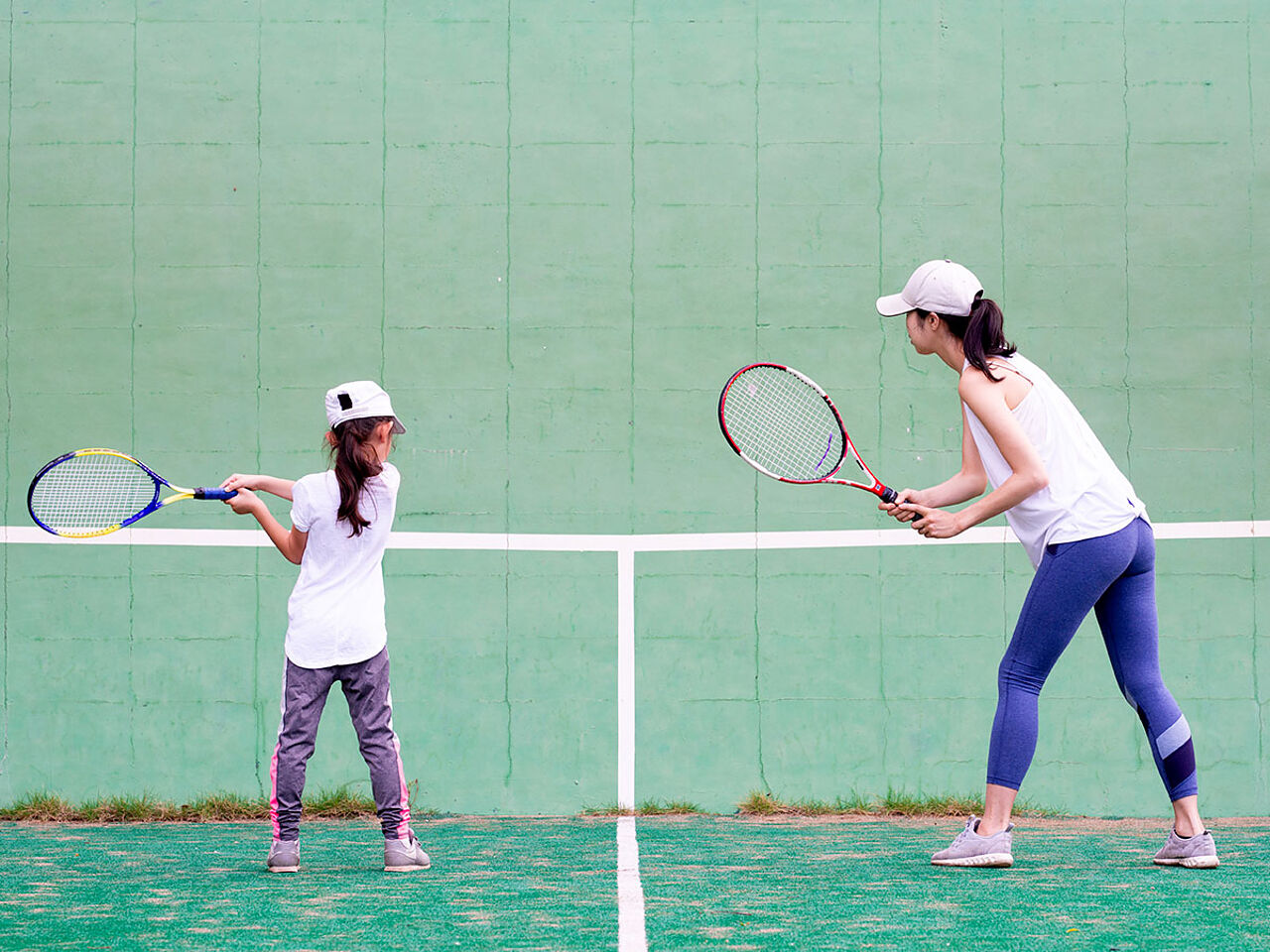 女性コーチにテニスの指導を受けている女の子の画像