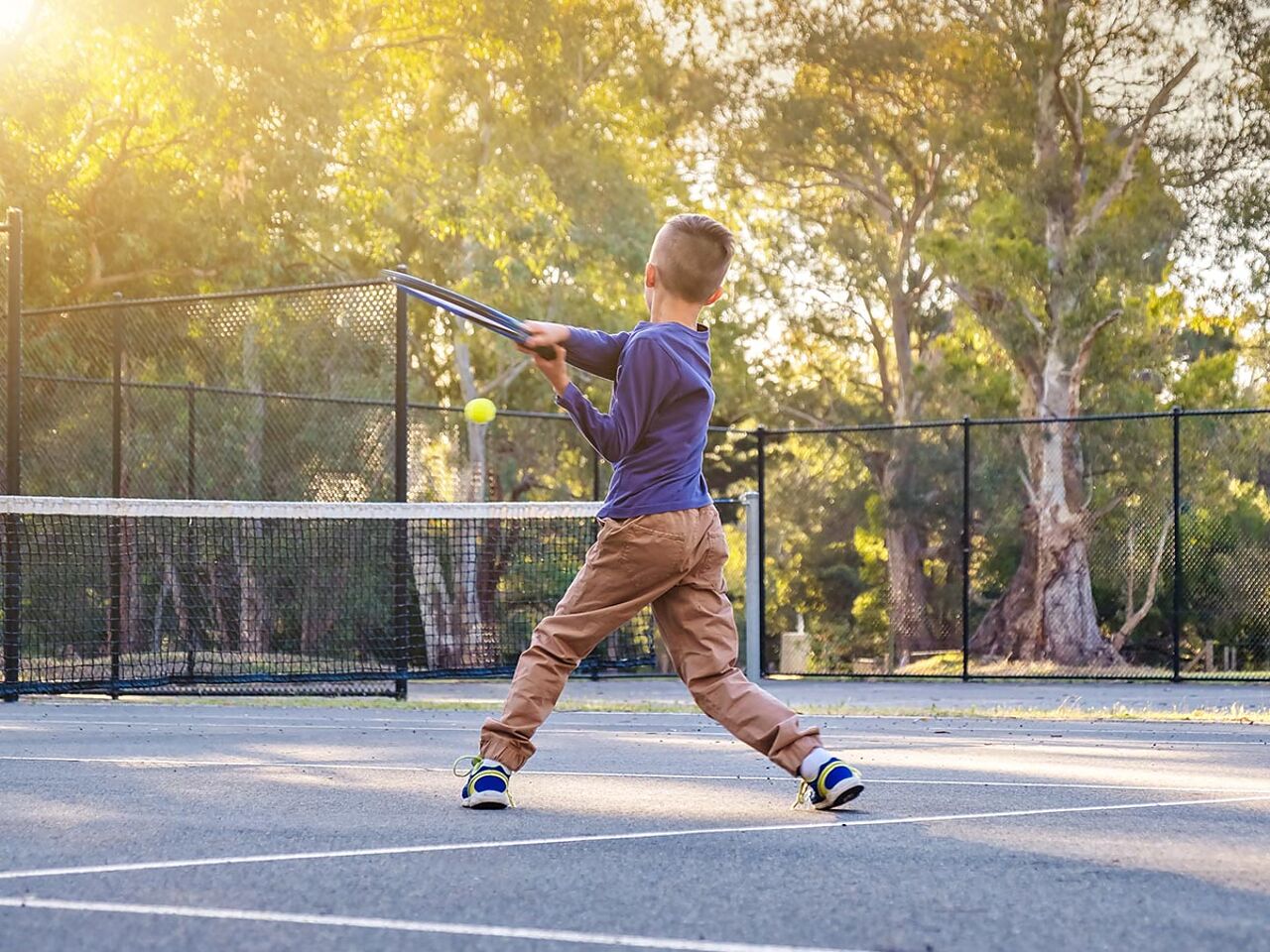 アウトドアコートでテニスをしている男の子の画像