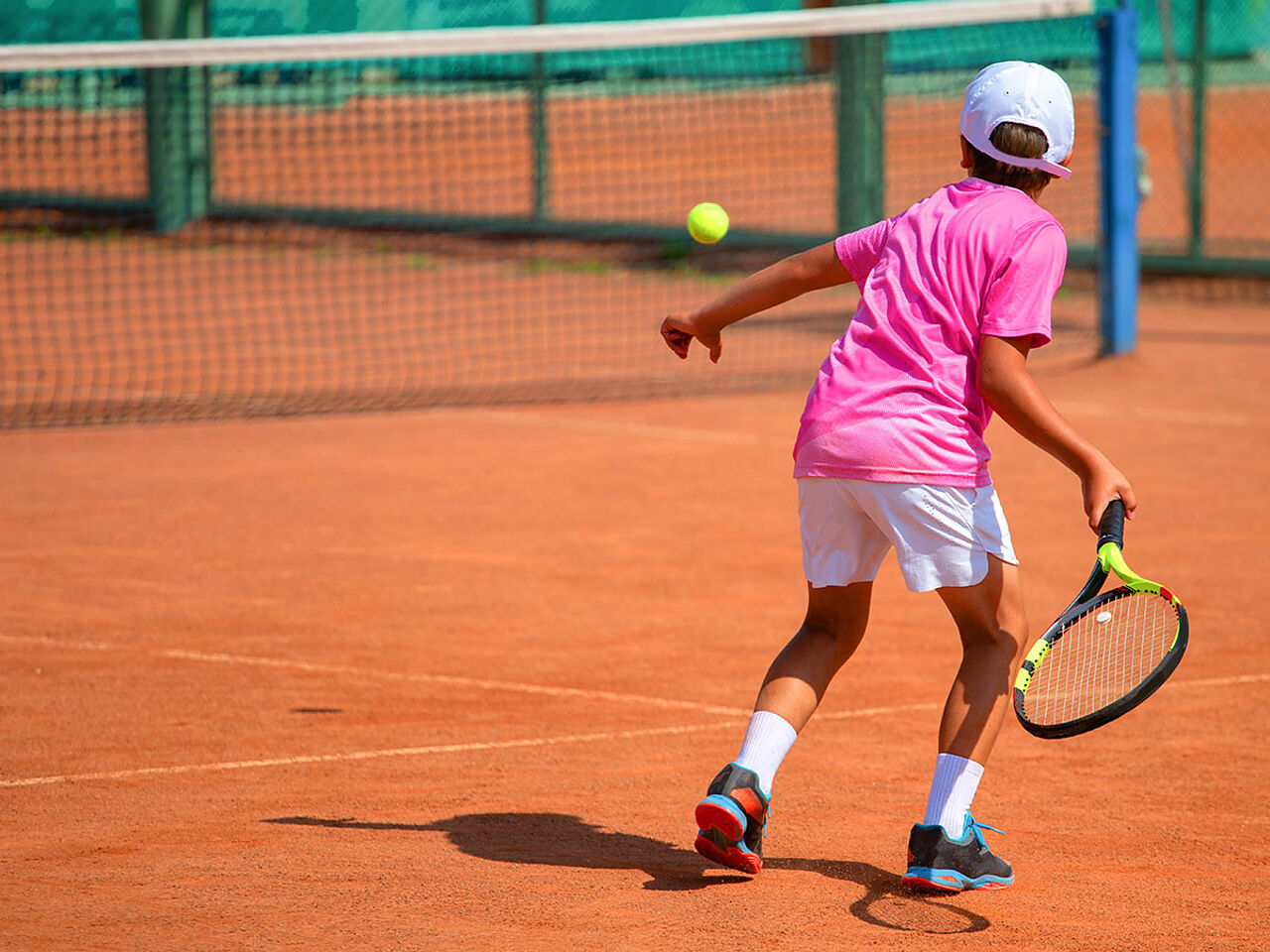 ピンクのテニスウェアを着た男の子がテニスをしている画像