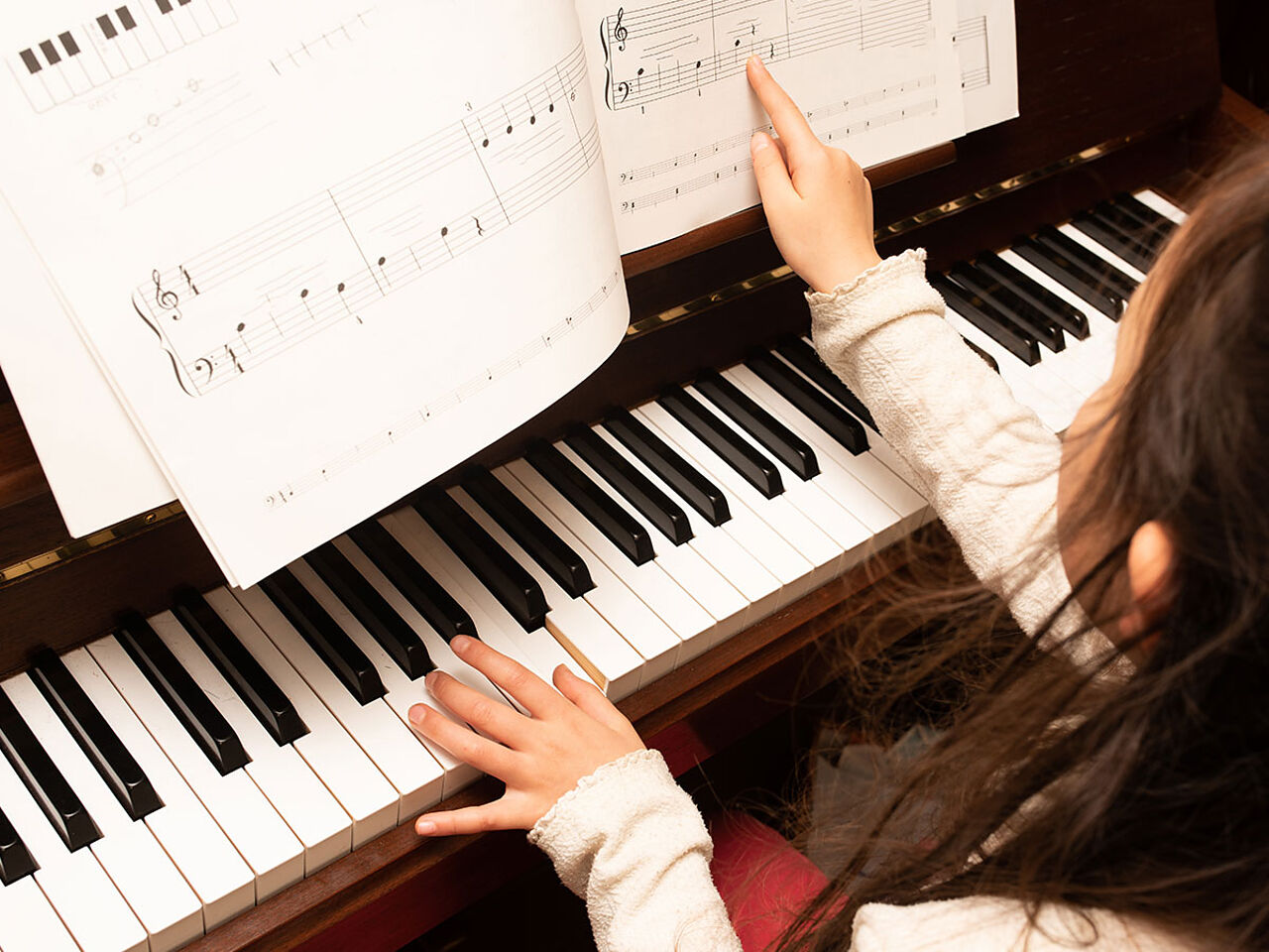 女の子が楽譜を見ながらピアノを弾いている画像