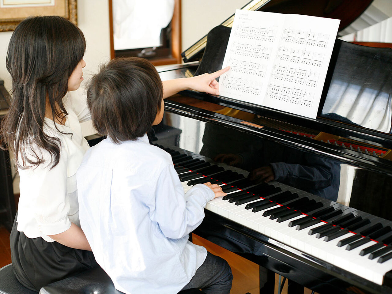 女性のピアノ講師に指導を受けている男の子の画像