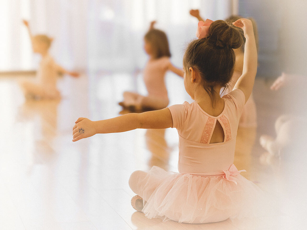 レオタードを着た幼児たちが座りながらバレエの手の動きの練習をしている画像
